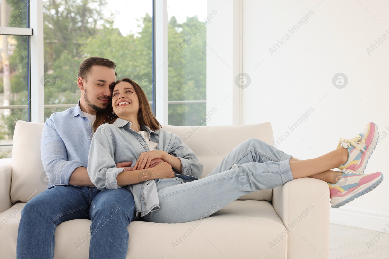 Photo of Man hugging his happy girlfriend on sofa at home