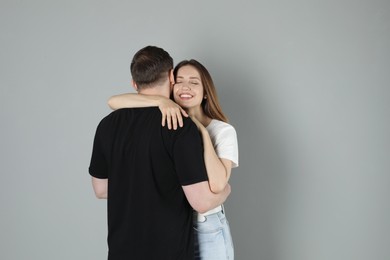 Smiling woman hugging her boyfriend on grey background. Space for text