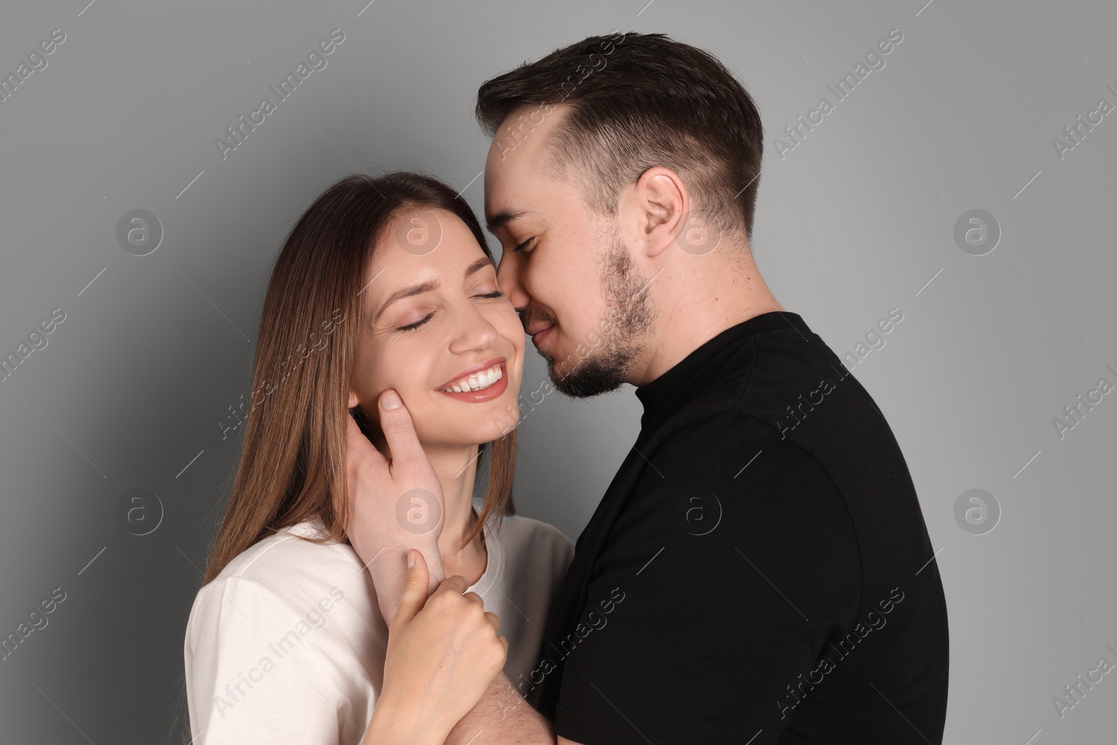 Photo of Man hugging and kissing his happy girlfriend on grey background