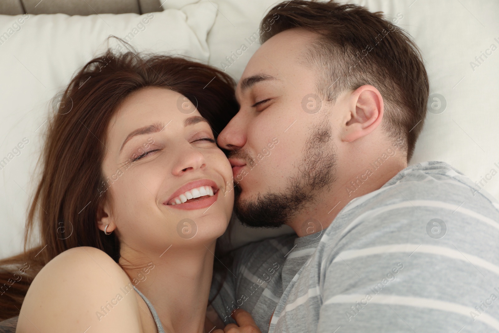 Photo of Man kissing his happy girlfriend on bed at home