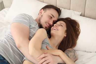 Photo of Man hugging his happy girlfriend on bed at home