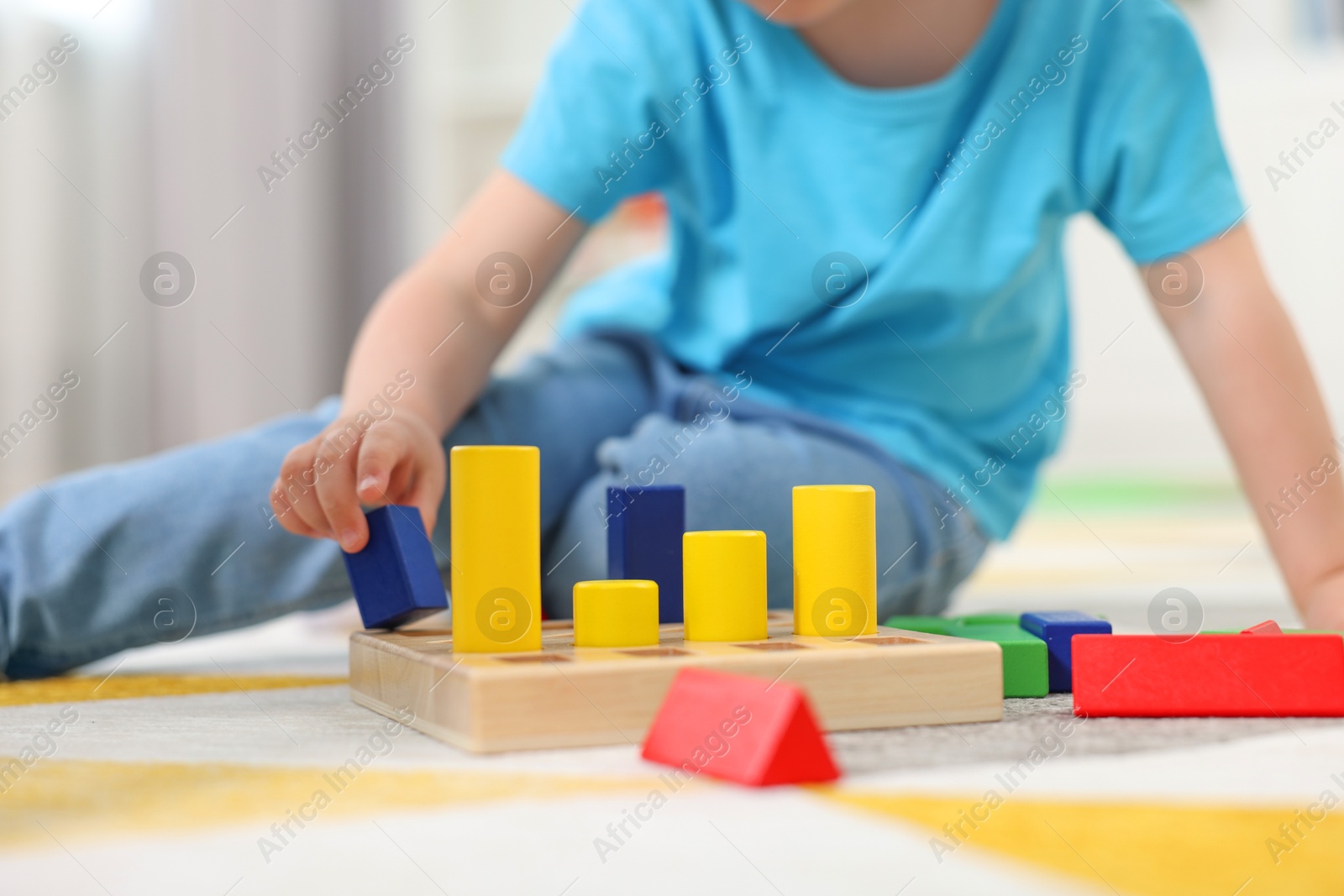 Photo of Little boy playing with set of wooden geometric figures on carpet, closeup. Kindergarten activities for motor skills development