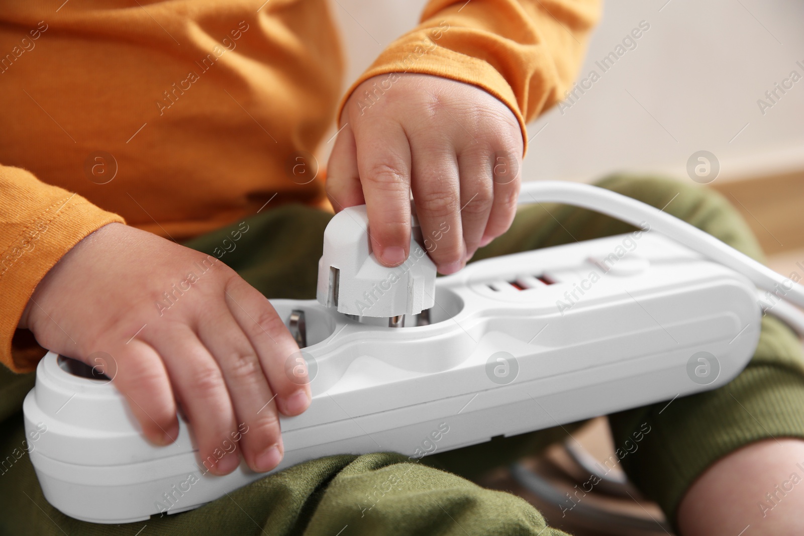 Photo of Little child playing with power strip and plug indoors, closeup