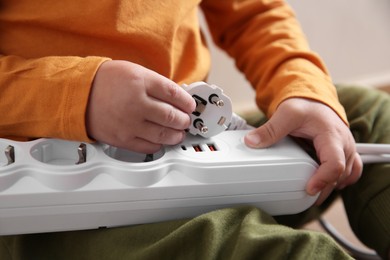 Little child playing with power strip and plug indoors, closeup