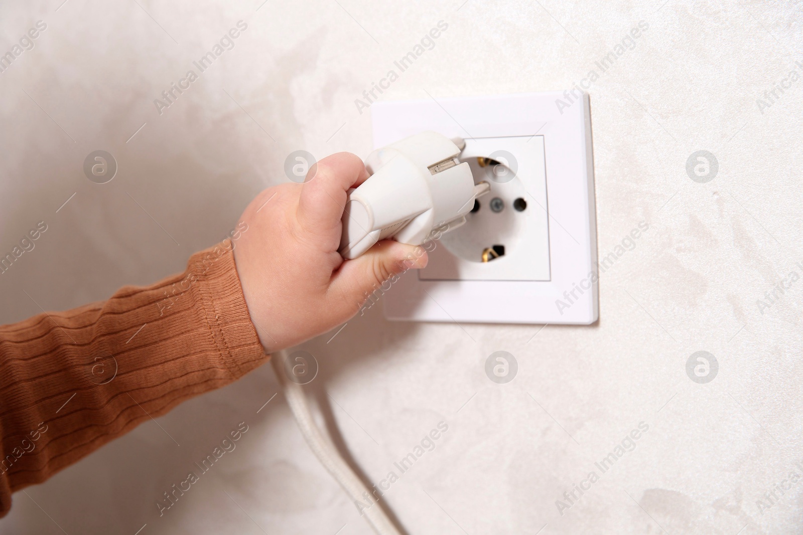 Photo of Little child playing with electrical socket and plug indoors, closeup. Dangerous situation