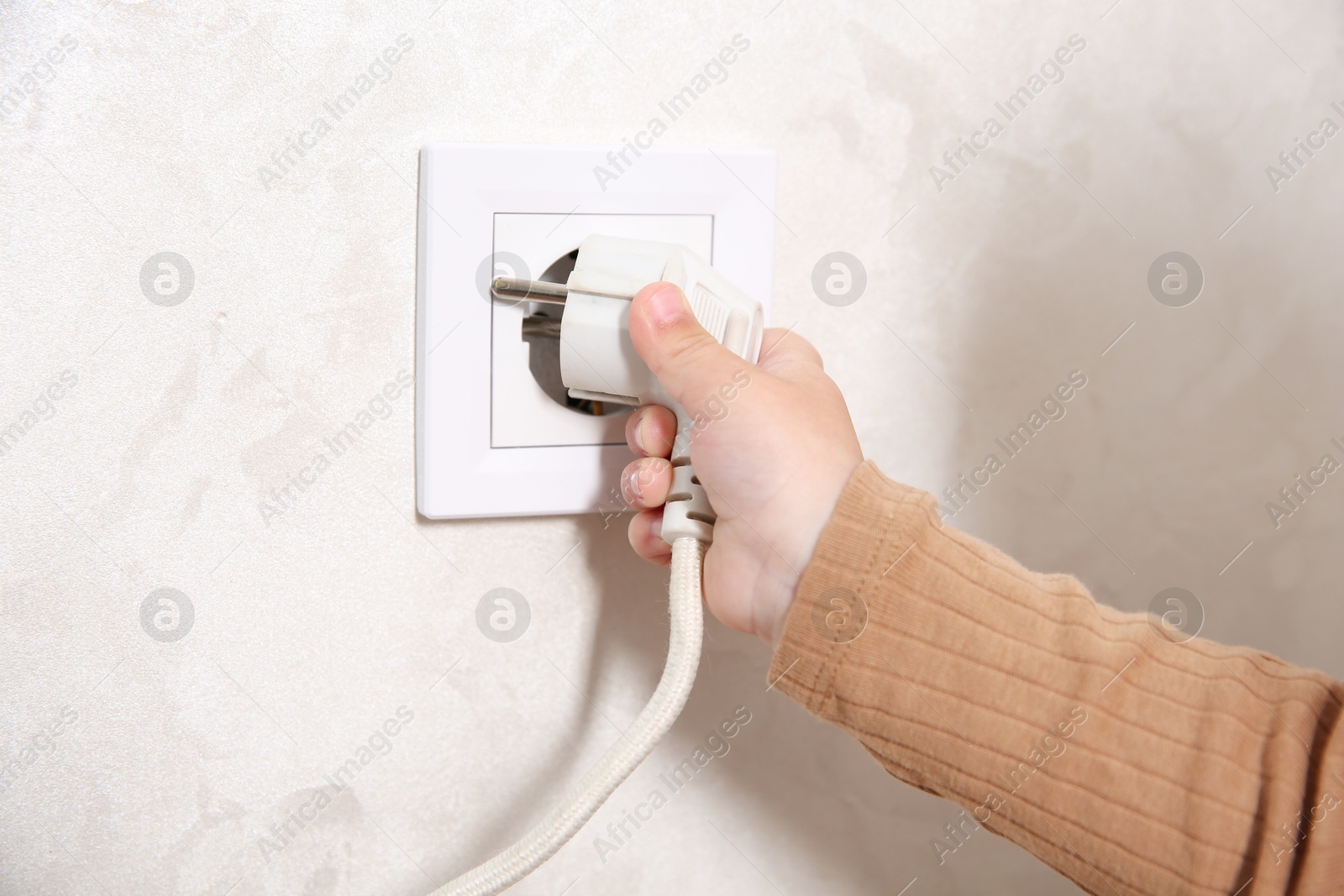 Photo of Little child playing with electrical socket and plug indoors, closeup. Dangerous situation