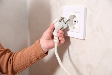 Photo of Little child playing with electrical socket and plug indoors, closeup. Dangerous situation