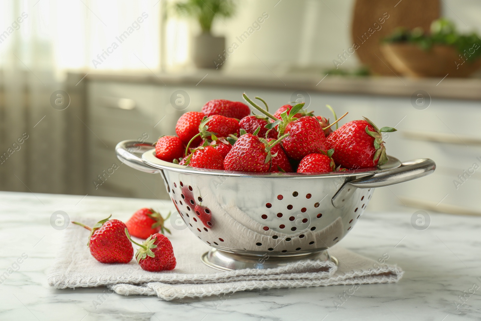 Photo of Metal colander with fresh strawberries on white marble table in kitchen