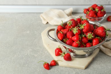 Metal colander with fresh strawberries on grey countertop, space for text