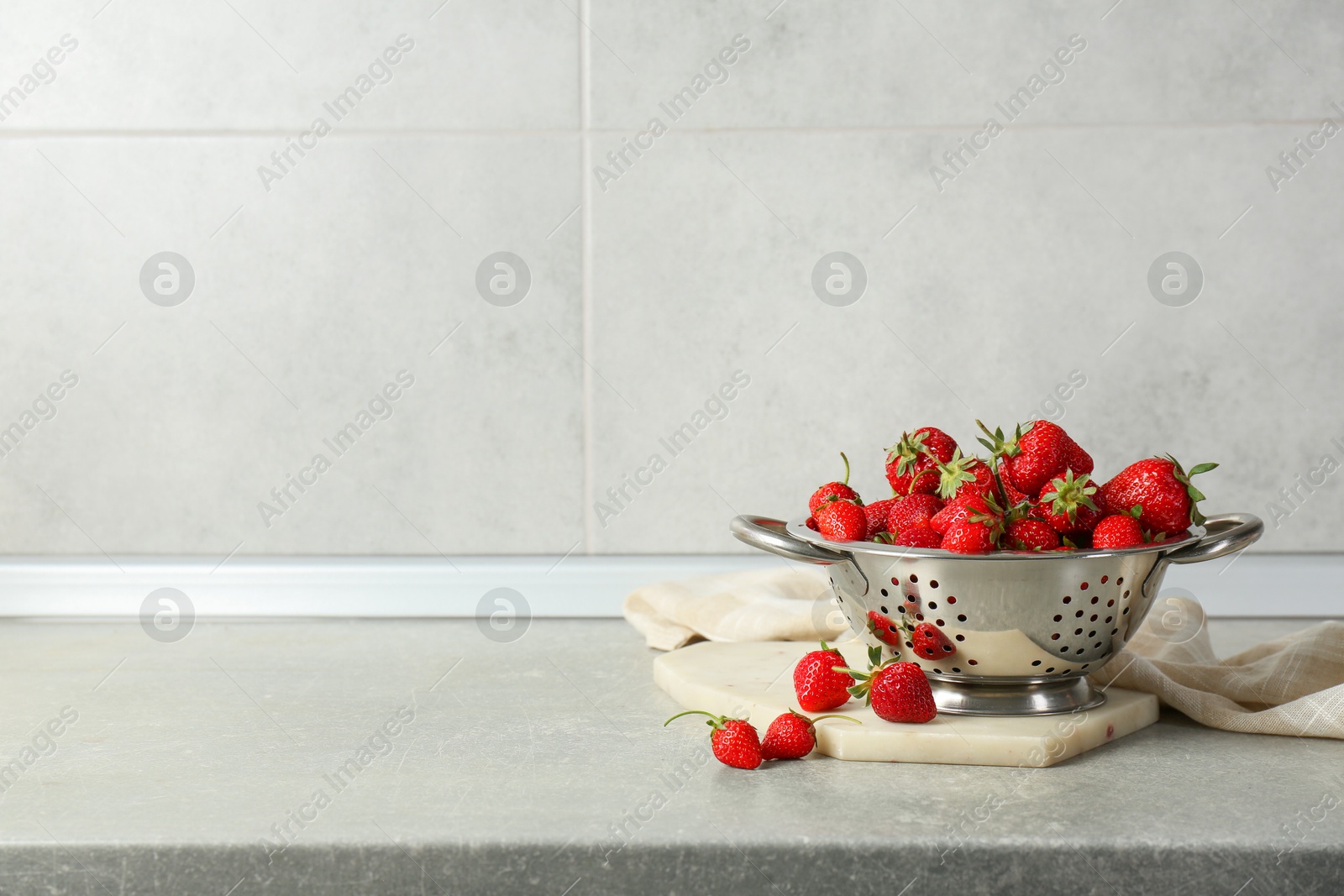 Photo of Metal colander with fresh strawberries on grey countertop, space for text