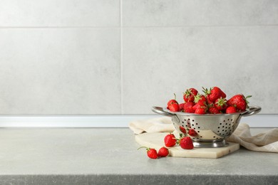 Photo of Metal colander with fresh strawberries on grey countertop, space for text