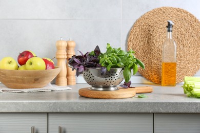 Metal colander with different fresh basil leaves and other products on grey countertop in kitchen