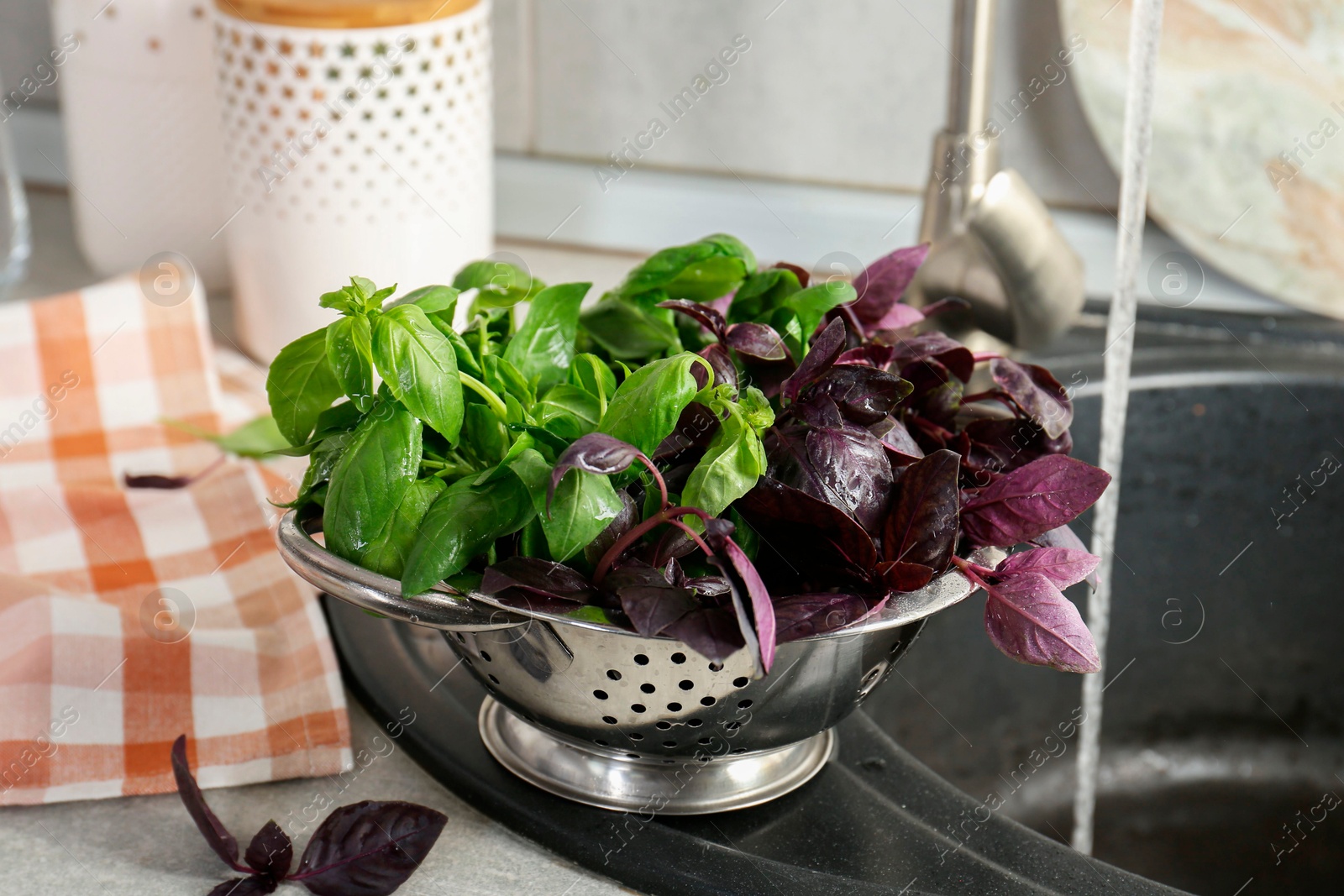 Photo of Metal colander with different fresh basil leaves on sink