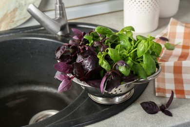 Photo of Metal colander with different fresh basil leaves on sink