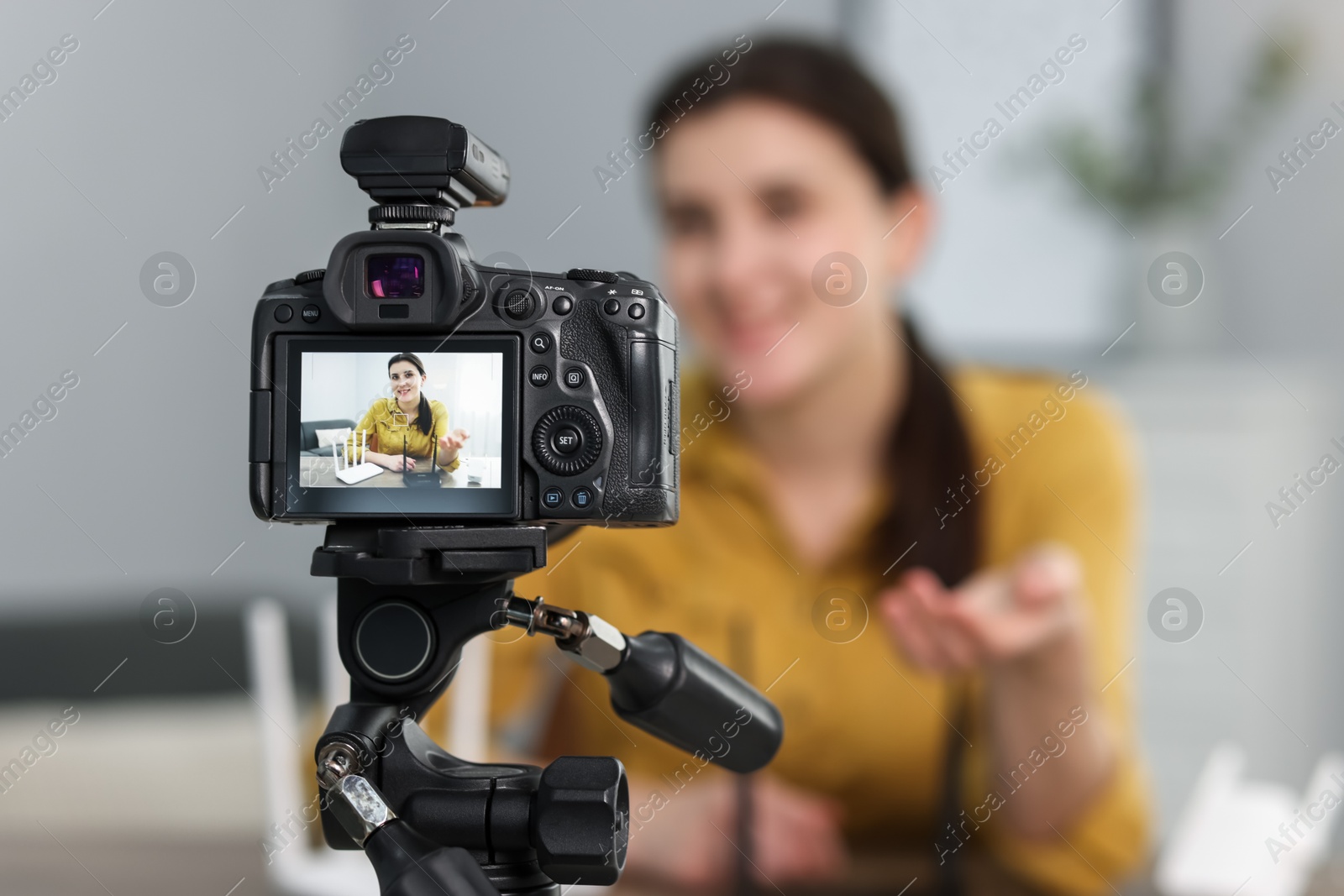 Photo of Technology blogger explaining something while recording video at home, focus on camera