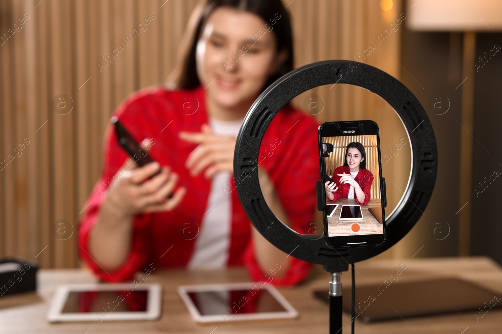 Photo of Technology blogger explaining something while recording video at home, focus on smartphone