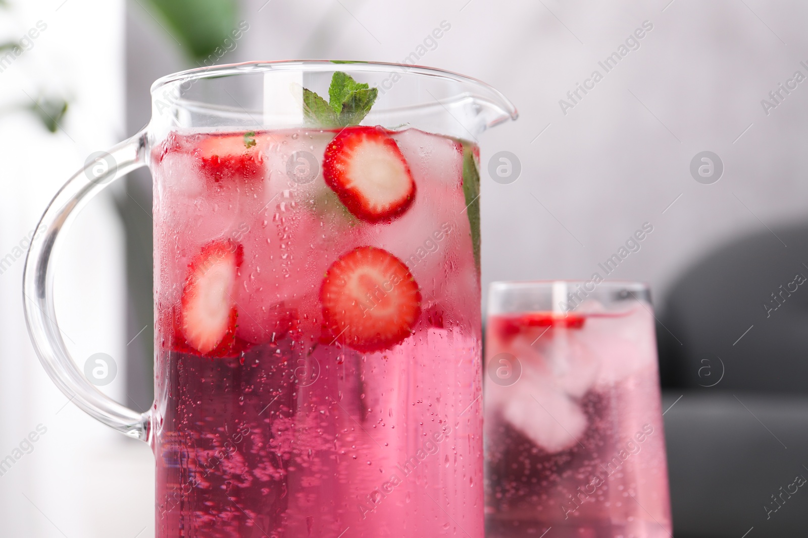 Photo of Freshly made strawberry lemonade with mint in jug and glass on table indoors, closeup