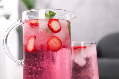 Freshly made strawberry lemonade with mint in jug and glass on table indoors, closeup