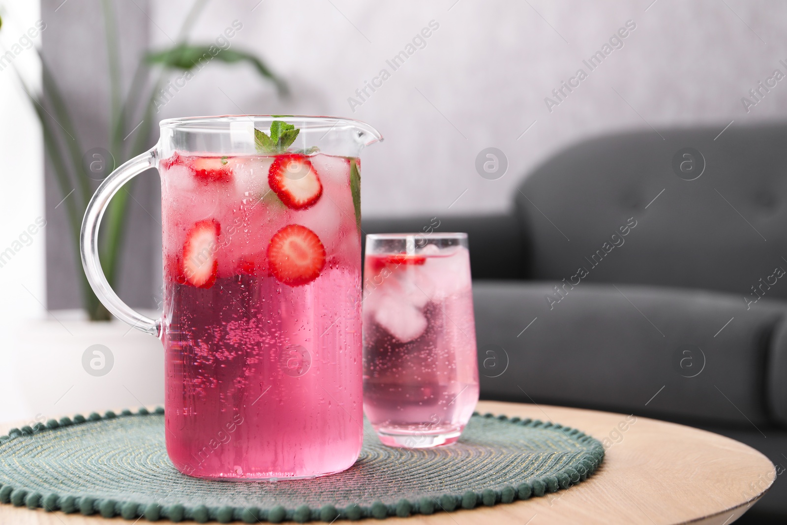 Photo of Freshly made strawberry lemonade with mint in jug and glass on wooden table indoors, space for text