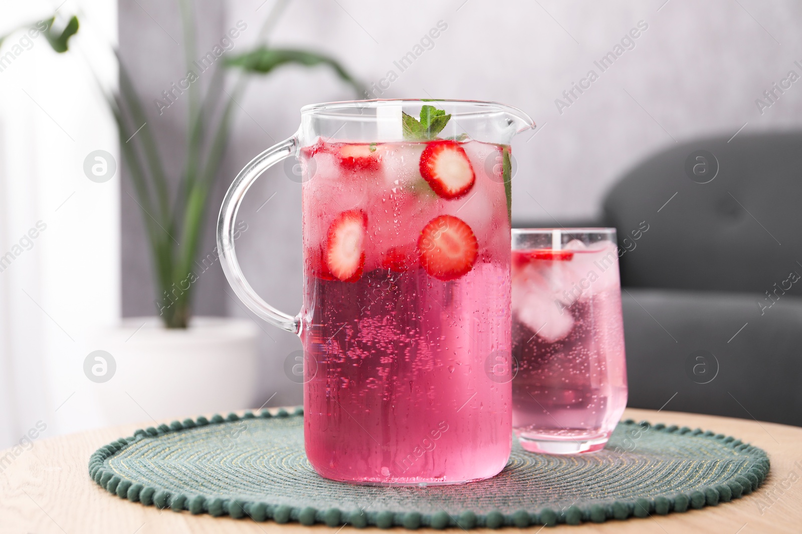 Photo of Freshly made strawberry lemonade with mint in jug and glass on wooden table indoors