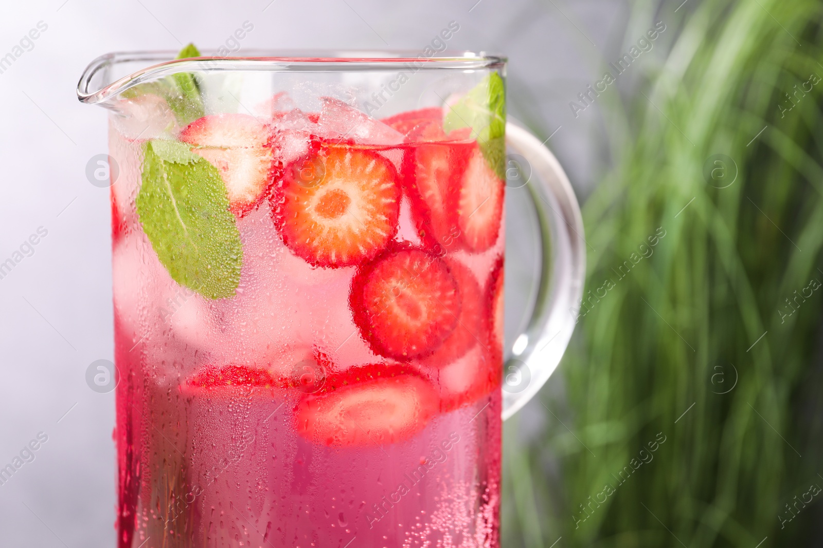 Photo of Freshly made strawberry lemonade with mint in jug and glass on grey background, closeup