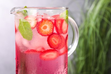 Photo of Freshly made strawberry lemonade with mint in jug and glass on grey background, closeup