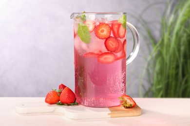 Photo of Freshly made strawberry lemonade with mint in jug and glass on white wooden table against grey background