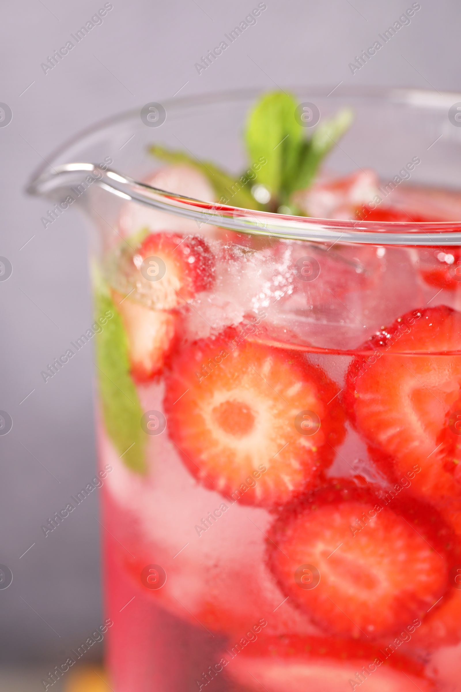 Photo of Freshly made strawberry lemonade with mint in jug and glass on grey background, closeup