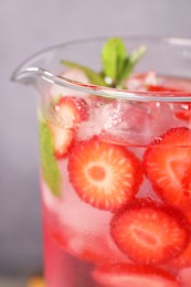 Photo of Freshly made strawberry lemonade with mint in jug and glass on grey background, closeup