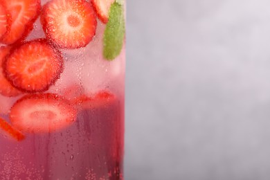 Photo of Freshly made strawberry lemonade with mint in jug and glass on grey background, closeup. Space for text