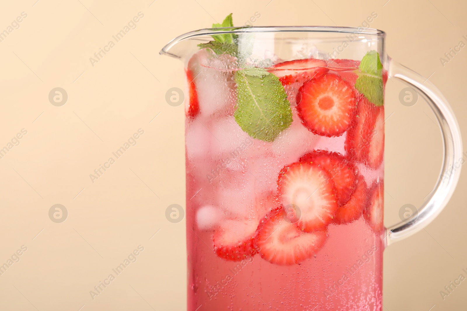 Photo of Freshly made strawberry lemonade with mint in jug on beige background, closeup. Space for text