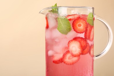 Photo of Freshly made strawberry lemonade with mint in jug on beige background, closeup. Space for text