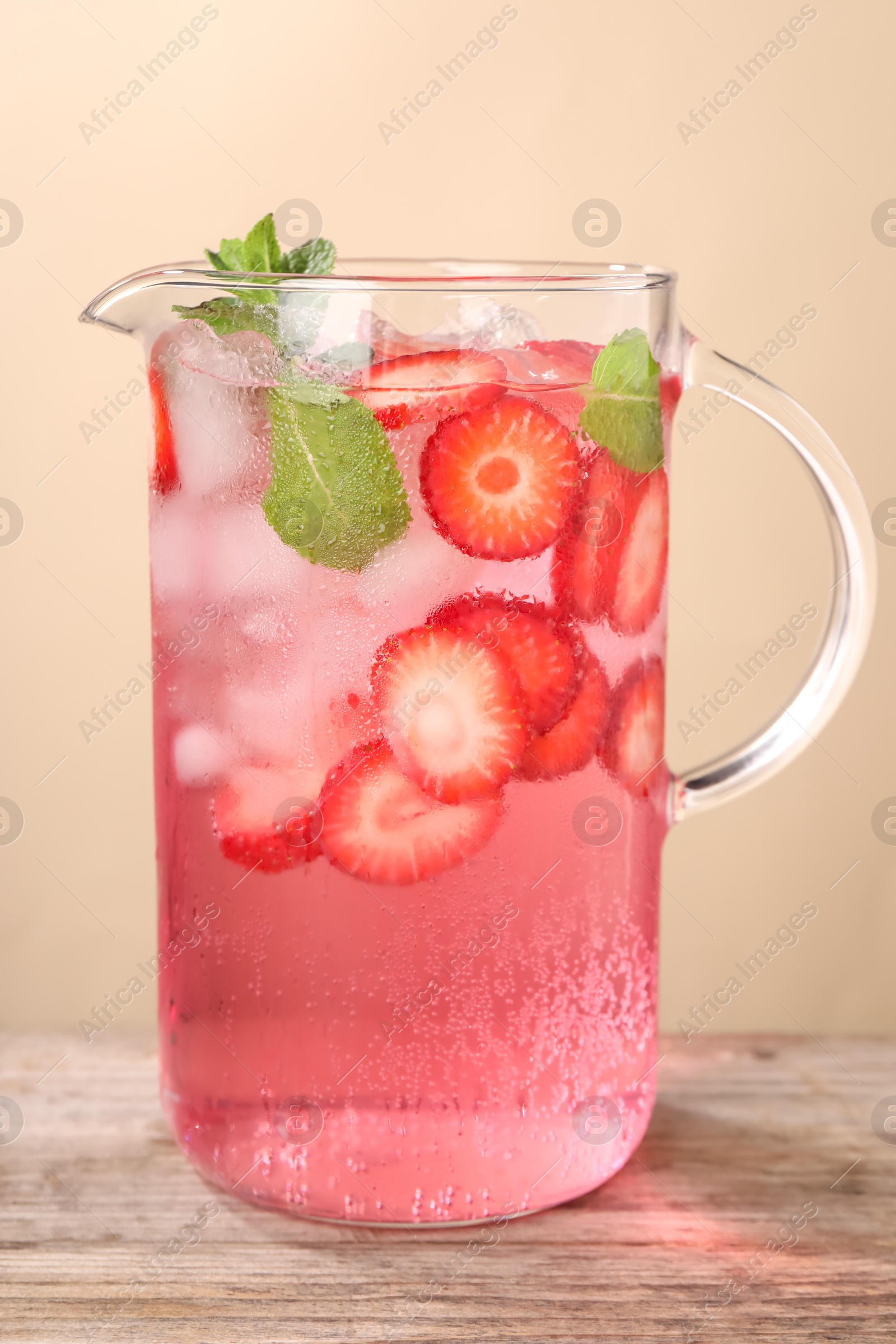 Photo of Freshly made strawberry lemonade with mint in jug on wooden table against beige background