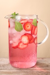 Freshly made strawberry lemonade with mint in jug on wooden table against beige background