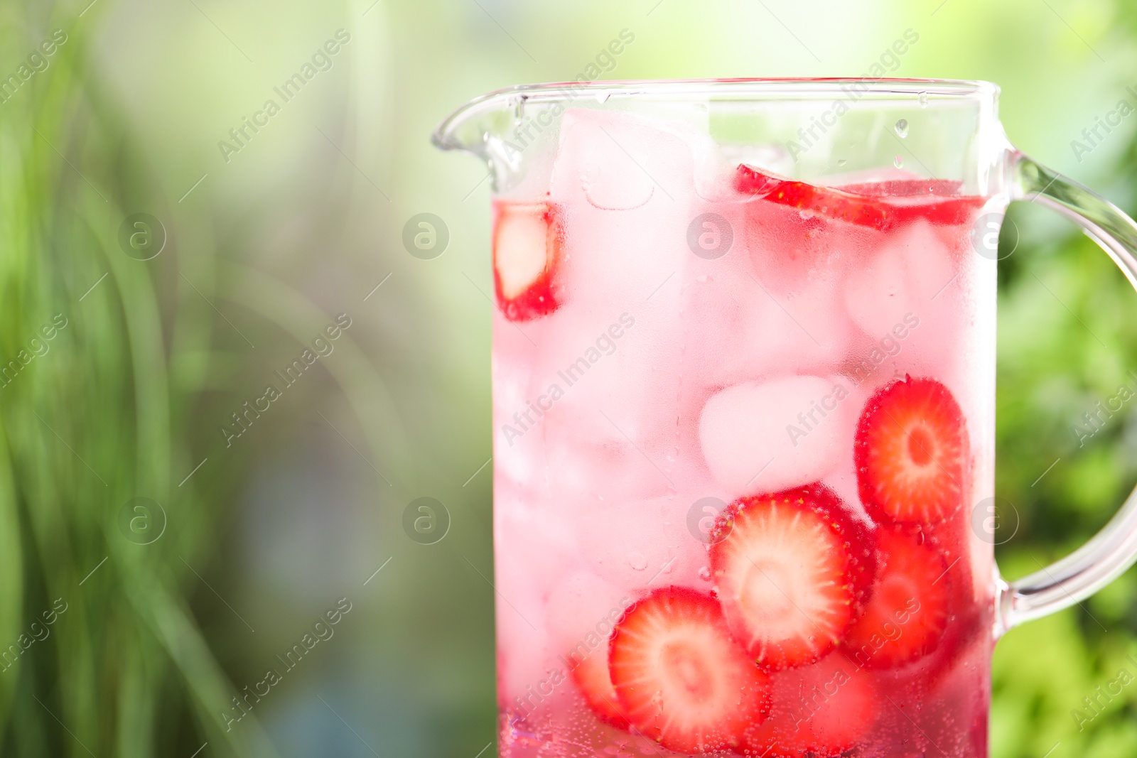 Photo of Freshly made strawberry lemonade in jug outdoors, closeup. Space for text