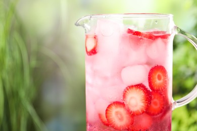 Photo of Freshly made strawberry lemonade in jug outdoors, closeup. Space for text