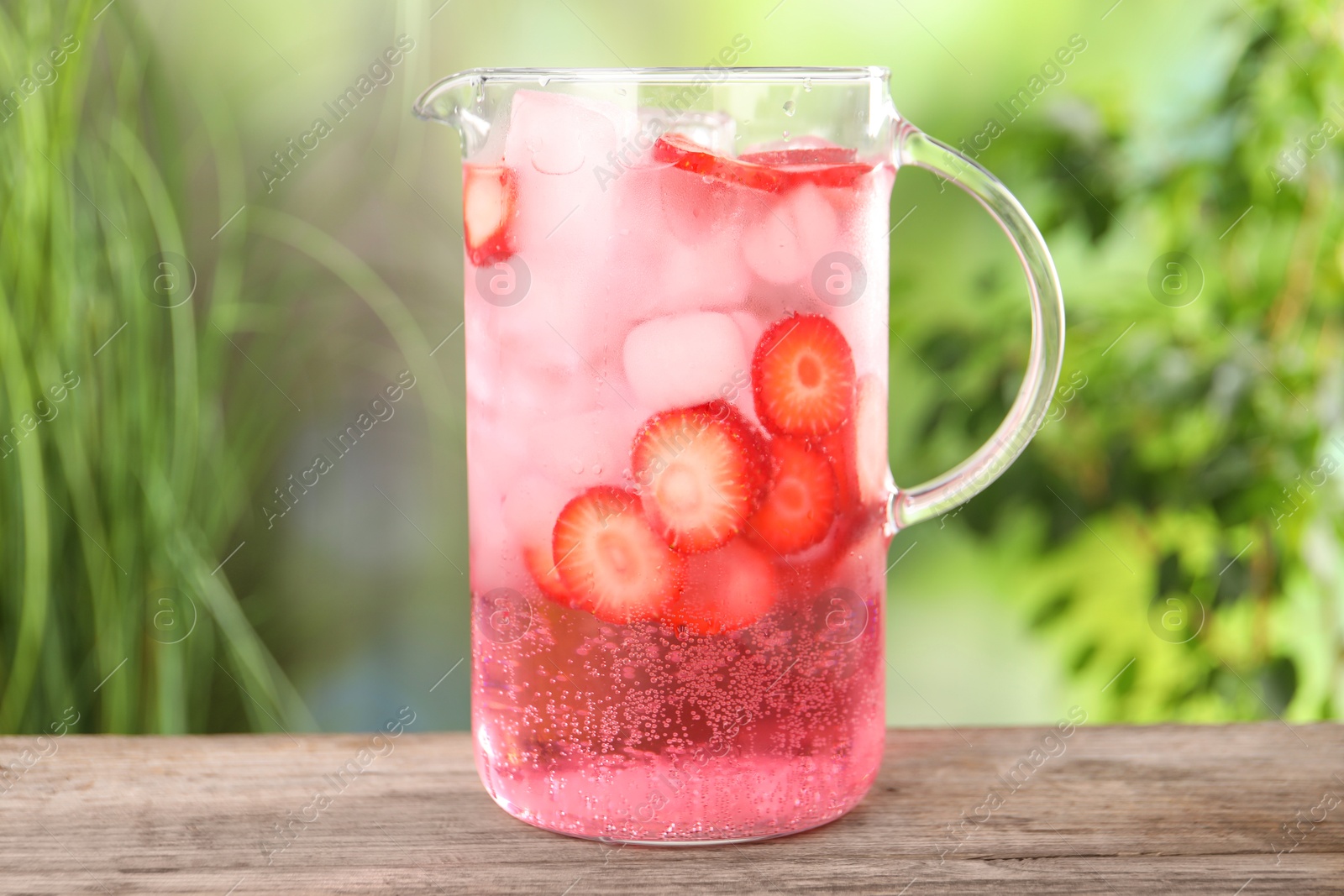 Photo of Freshly made strawberry lemonade in jug on wooden table outdoors