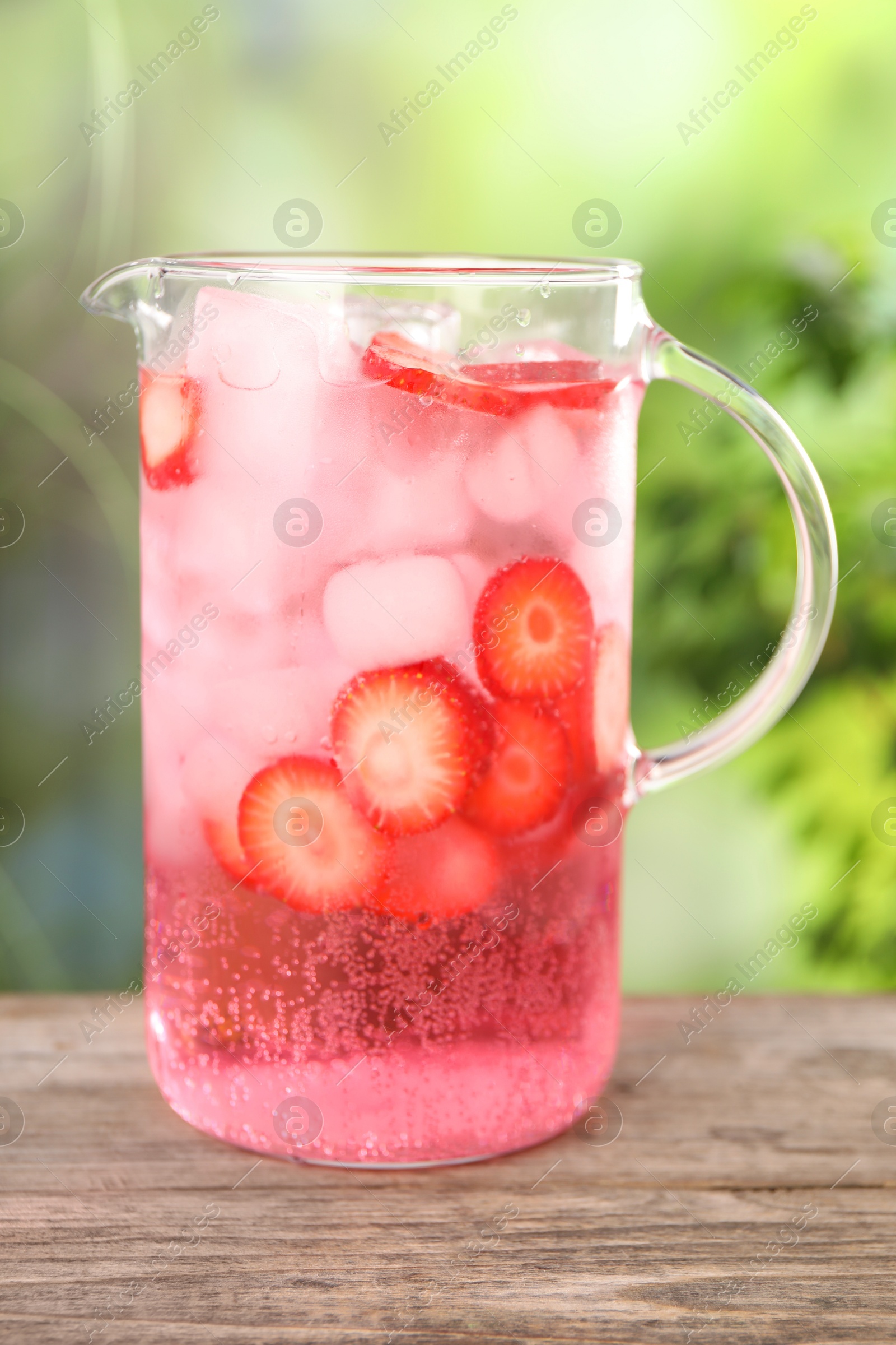 Photo of Freshly made strawberry lemonade in jug on wooden table outdoors