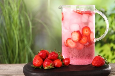 Freshly made strawberry lemonade in jug on wooden table outdoors, space for text