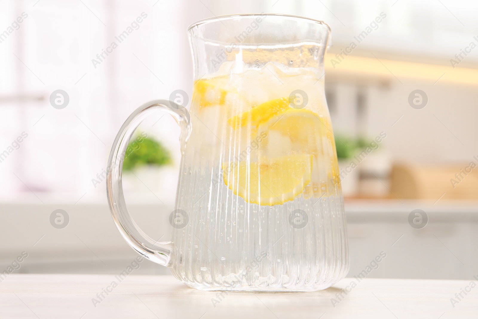 Photo of Freshly made lemonade in jug on white wooden table indoors