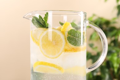 Freshly made lemonade with mint in jug on beige background, closeup