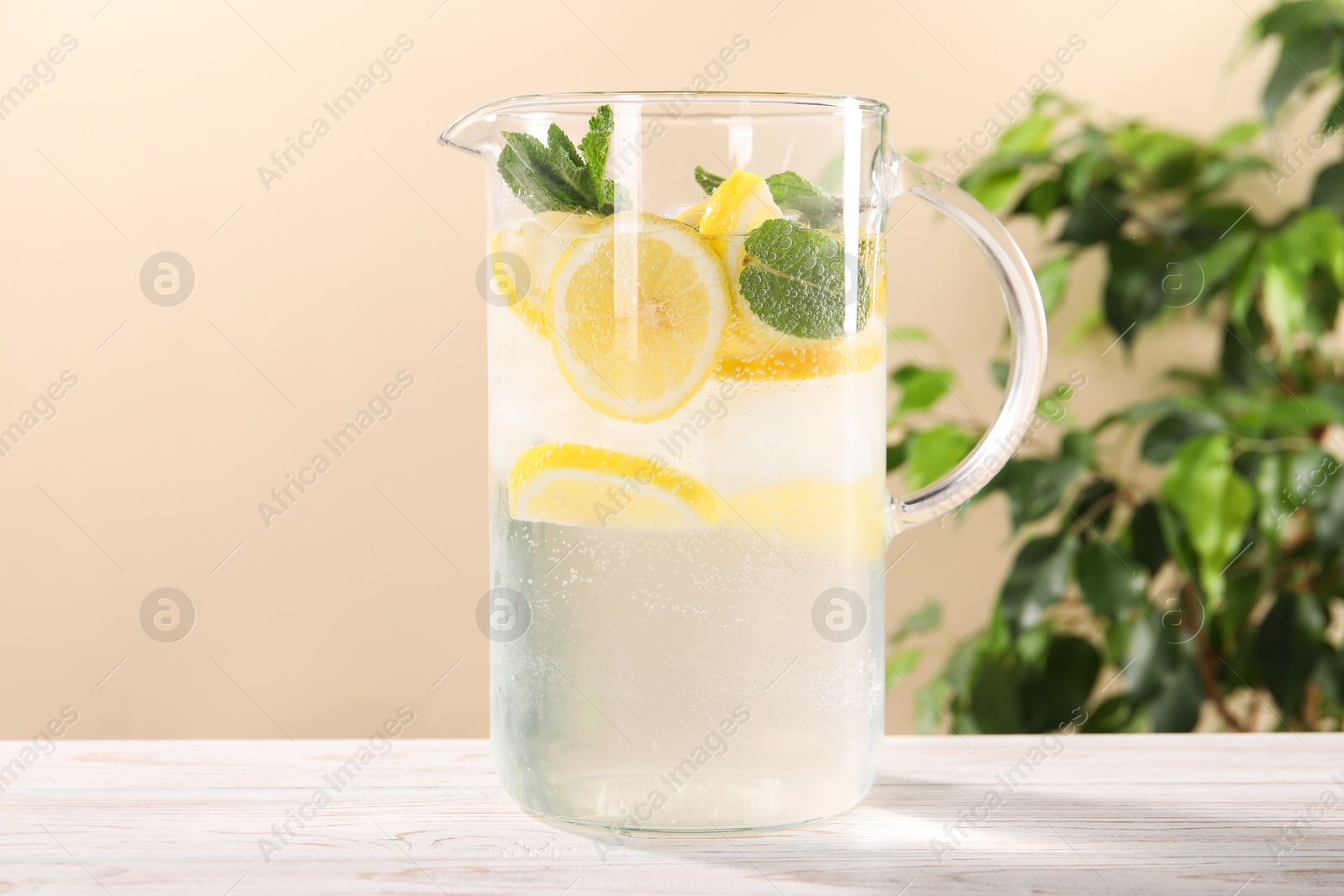 Photo of Freshly made lemonade with mint in jug on white wooden table against beige background