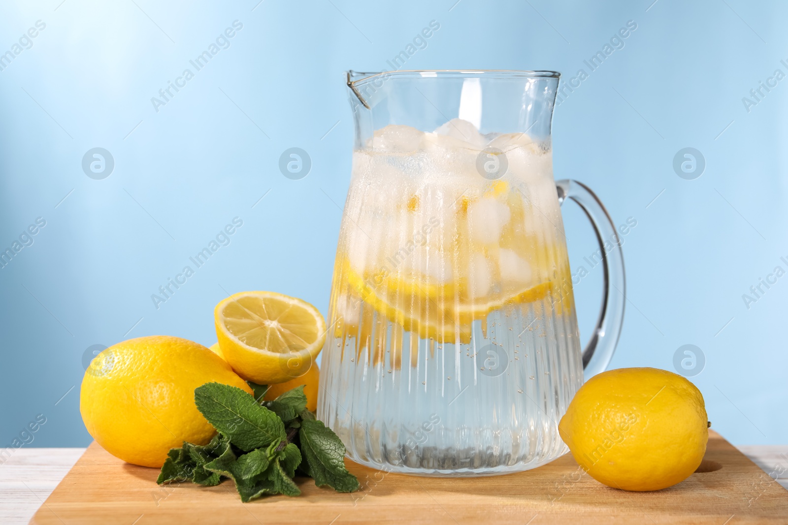 Photo of Freshly made lemonade with mint in jug on white wooden table against light blue background