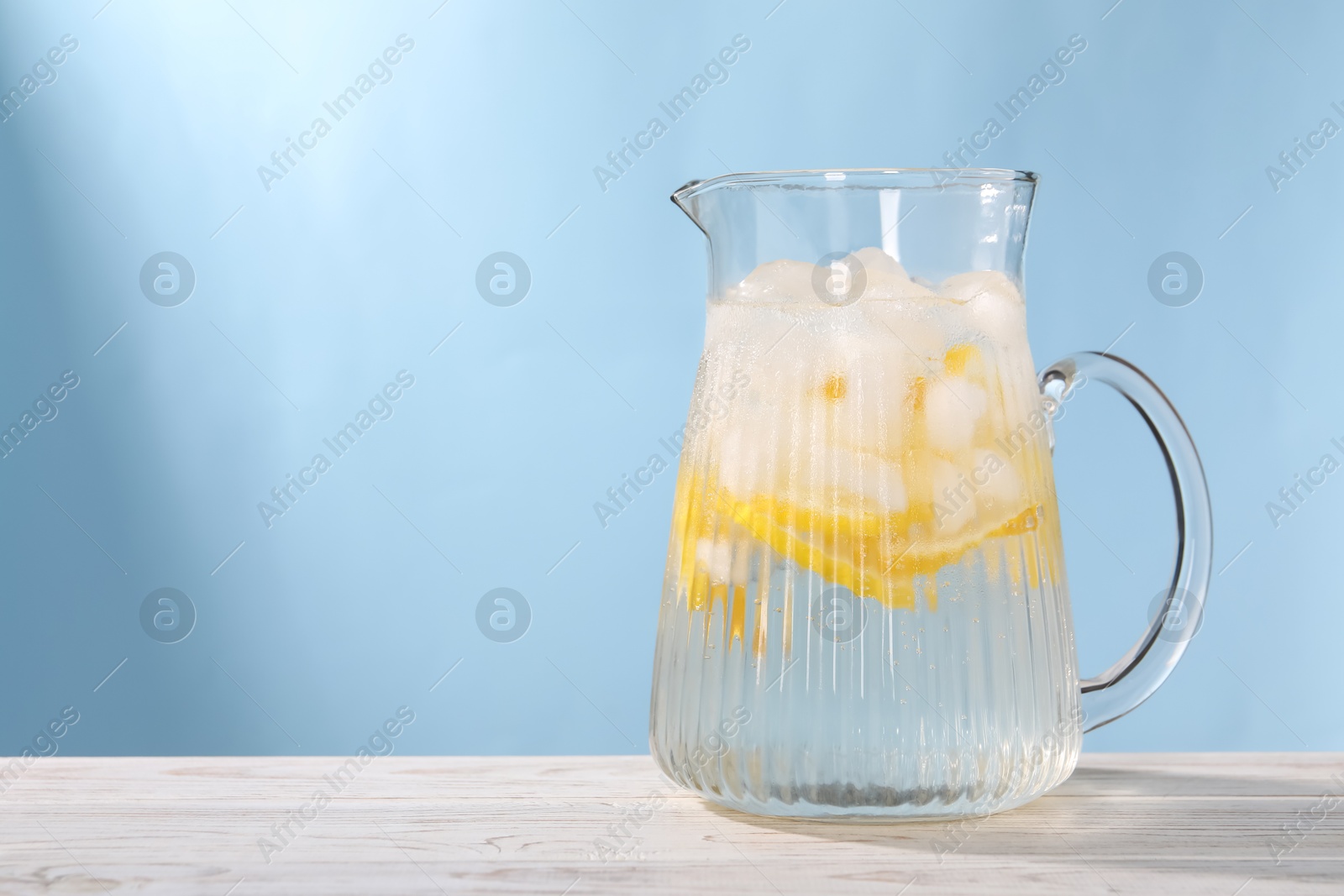 Photo of Freshly made lemonade in jug on white wooden table against light blue background, space for text