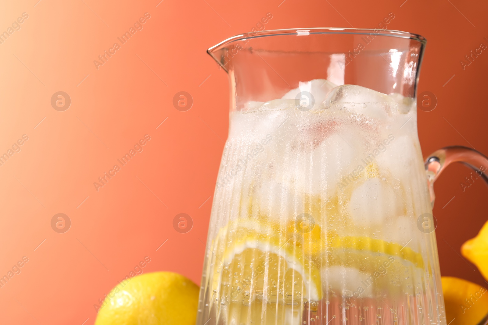 Photo of Freshly made lemonade in jug on orange background, closeup. Space for text