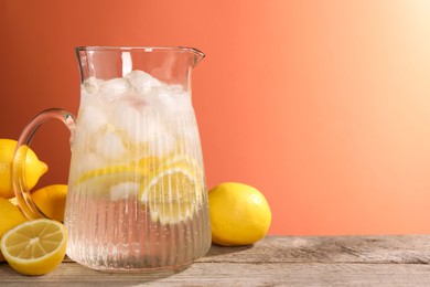 Photo of Freshly made lemonade in jug on wooden table against orange background, space for text