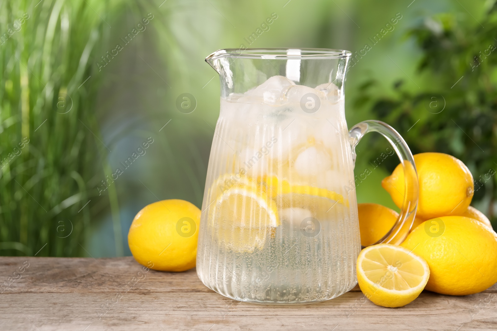 Photo of Freshly made lemonade in jug on wooden table outdoors