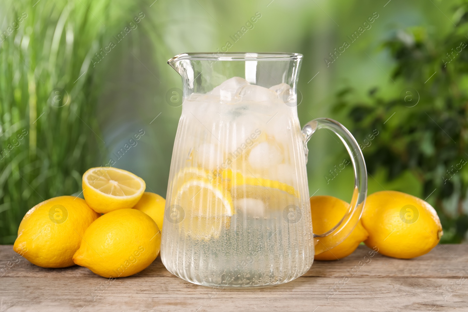 Photo of Freshly made lemonade in jug on wooden table outdoors