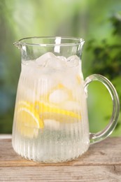 Photo of Freshly made lemonade in jug on wooden table outdoors