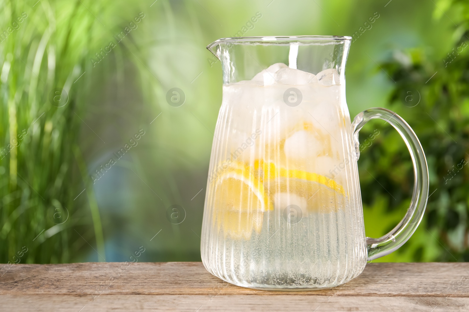 Photo of Freshly made lemonade in jug on wooden table outdoors, space for text